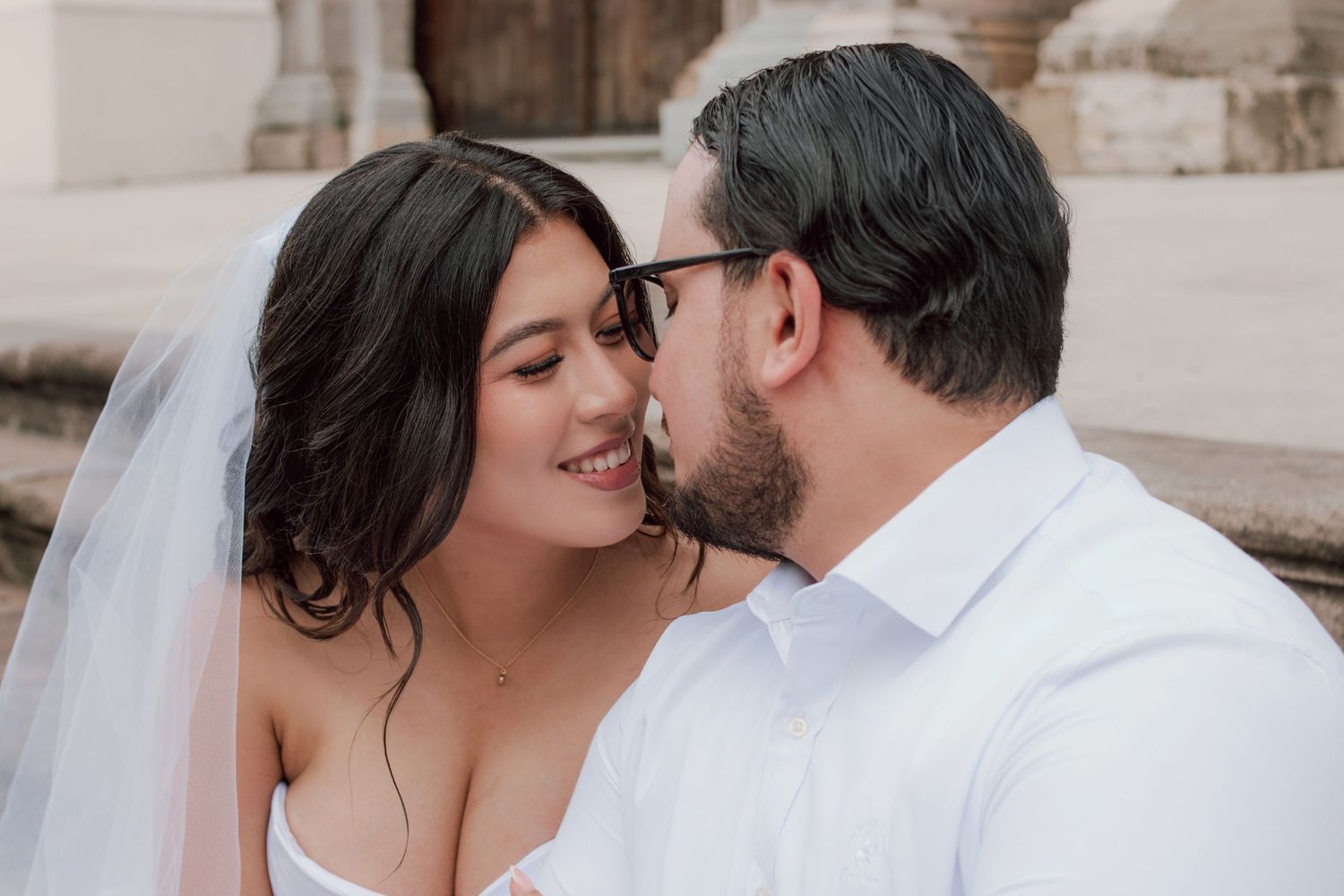 A romantic wedding moment captured between newlyweds in front of stone architecture.