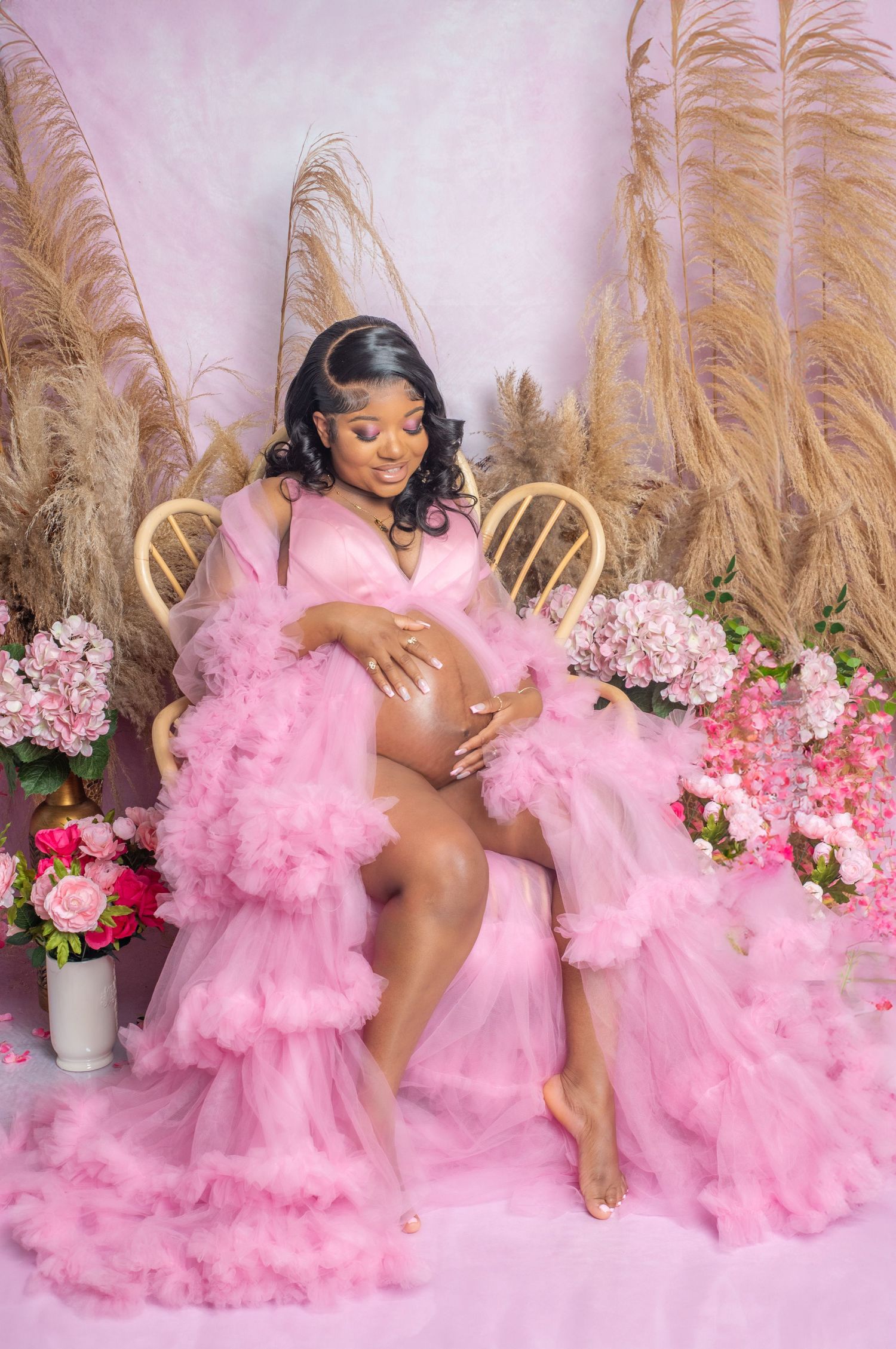 A pink tulle maternity photo session setup with floral arrangements and pampas grass decorations in the background.
