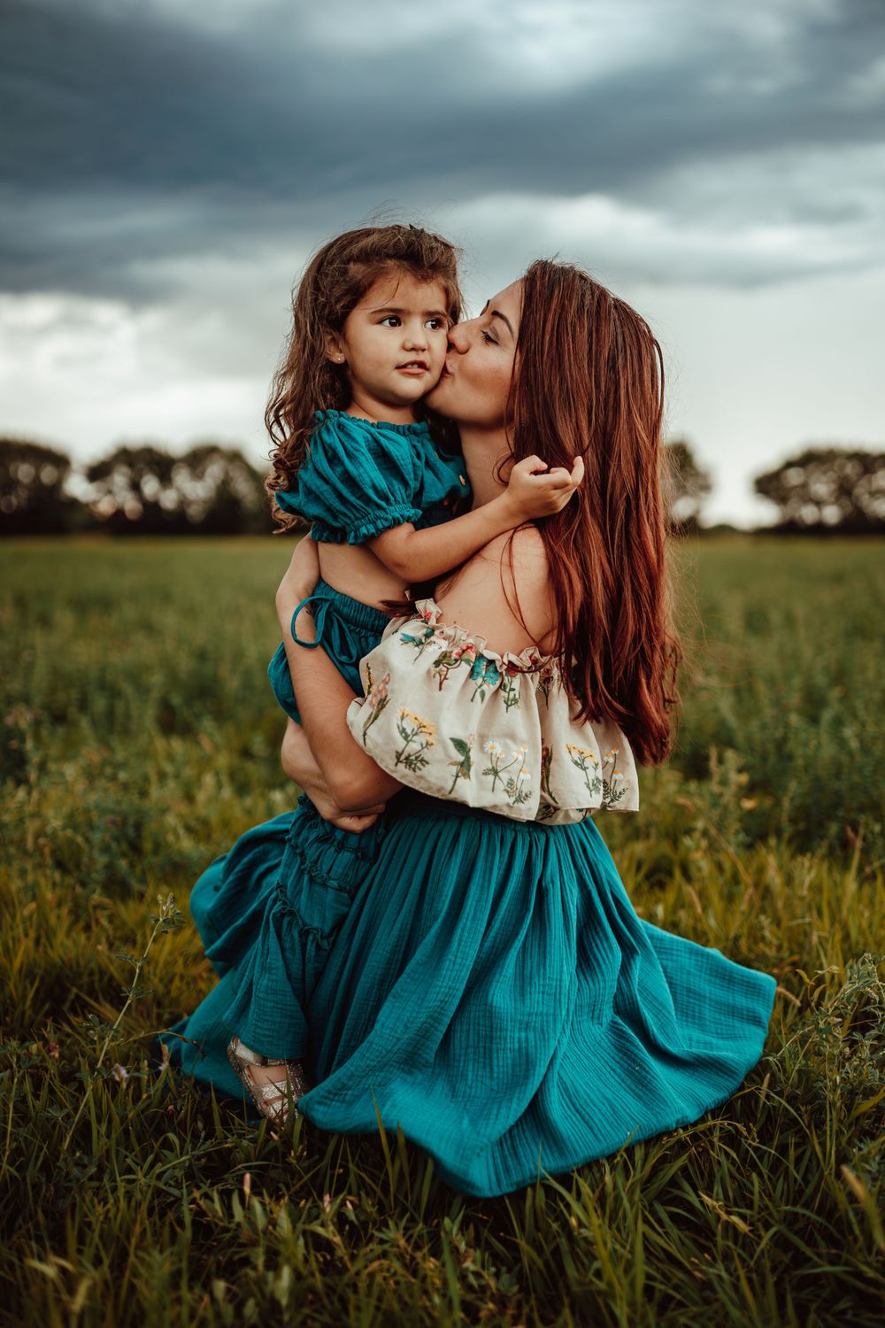 Tender moment between parent and child in coordinating teal outfits in a green field.