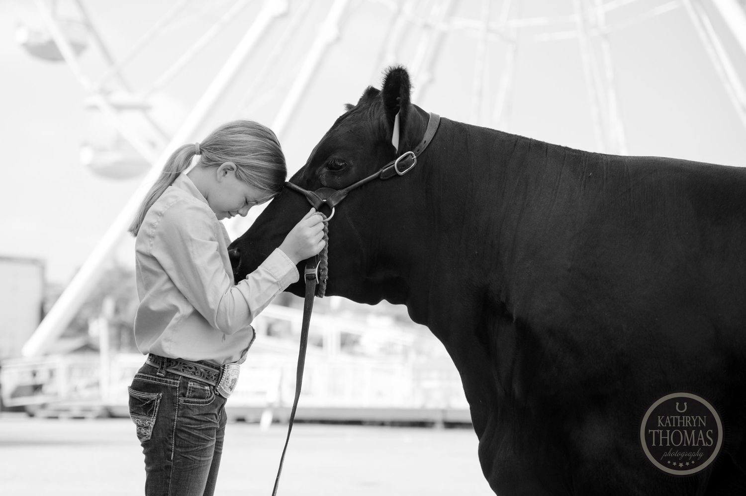 Black and white image of a young exhibitor bonding with their show animal near a ferris wheel.