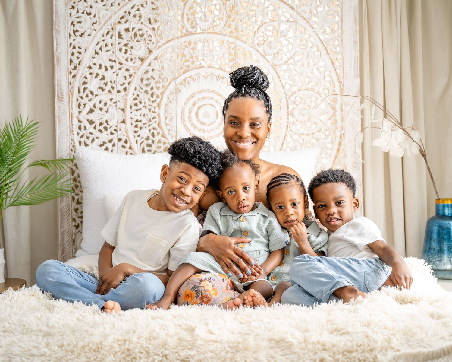 Family portrait of siblings sitting together on white fur rug against ornate mandala wall decor.