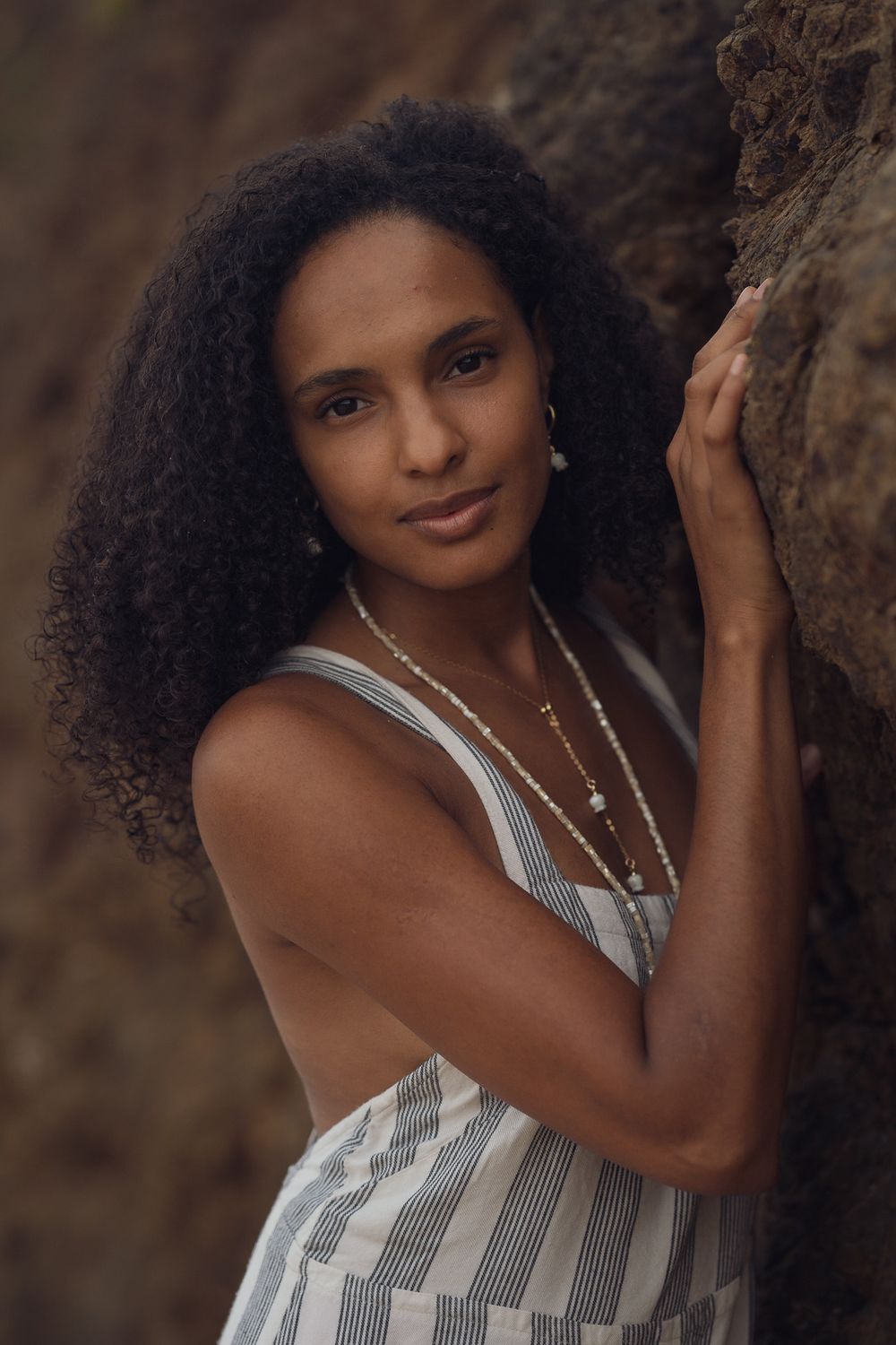 Striped summer dress with layered necklaces photographed against rocky beach setting.