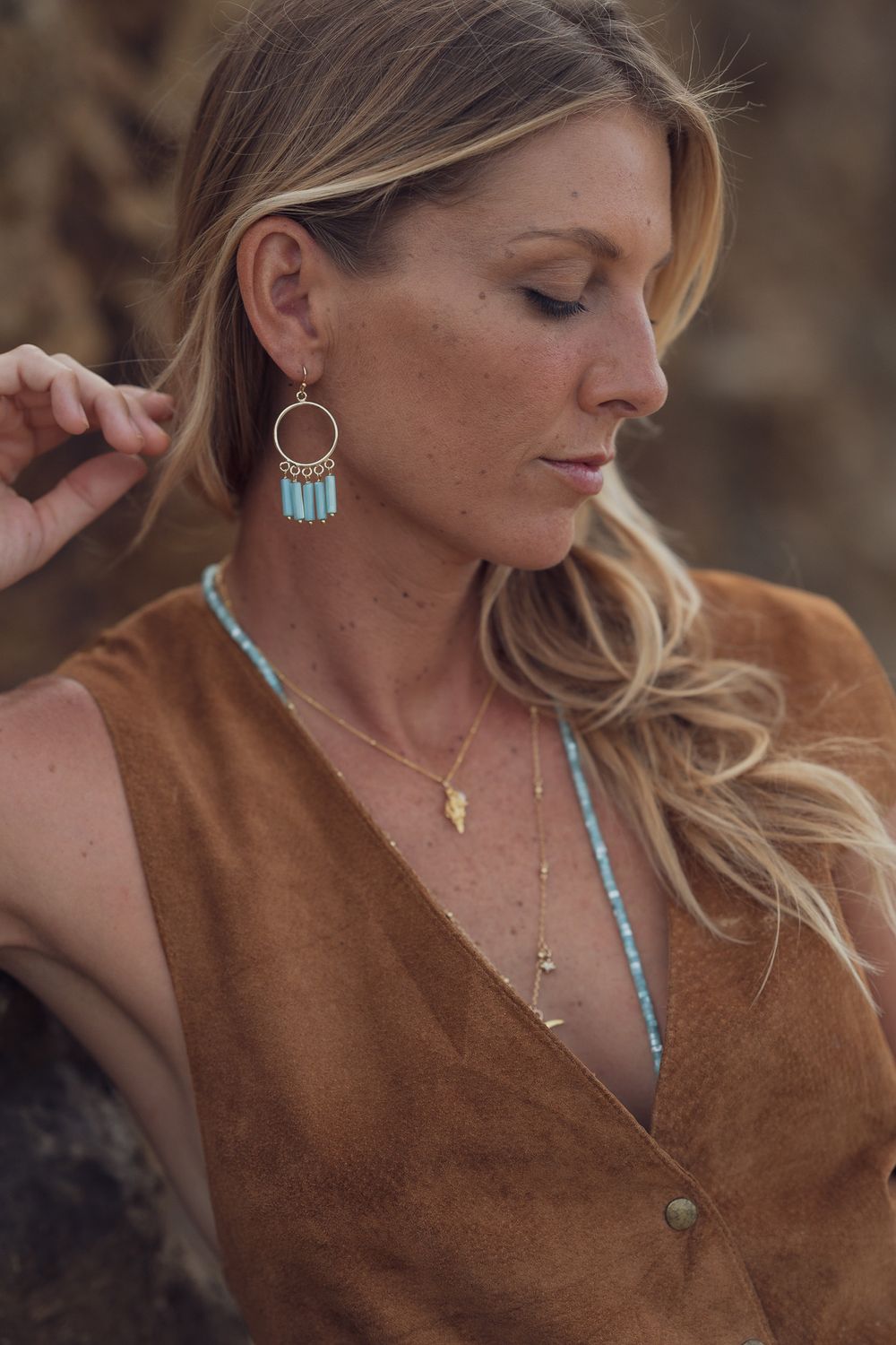 A close-up portrait shows delicate turquoise jewelry paired with a brown suede top in warm natural lighting.
