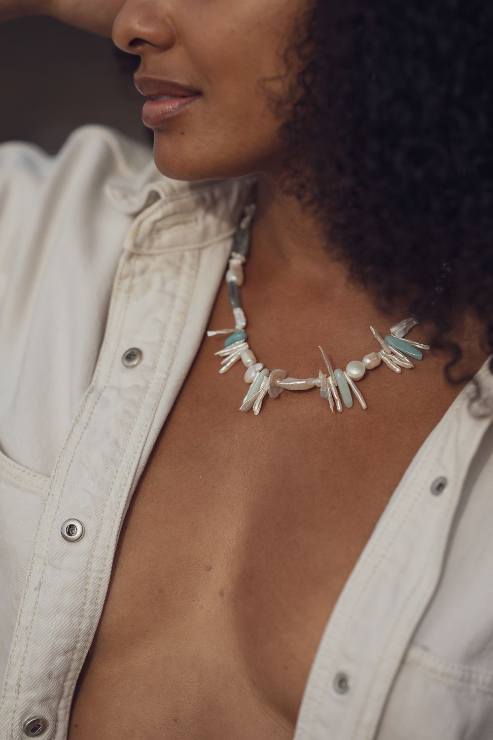 Close-up detail of a white spiked turquoise statement necklace worn with a white button-down shirt.