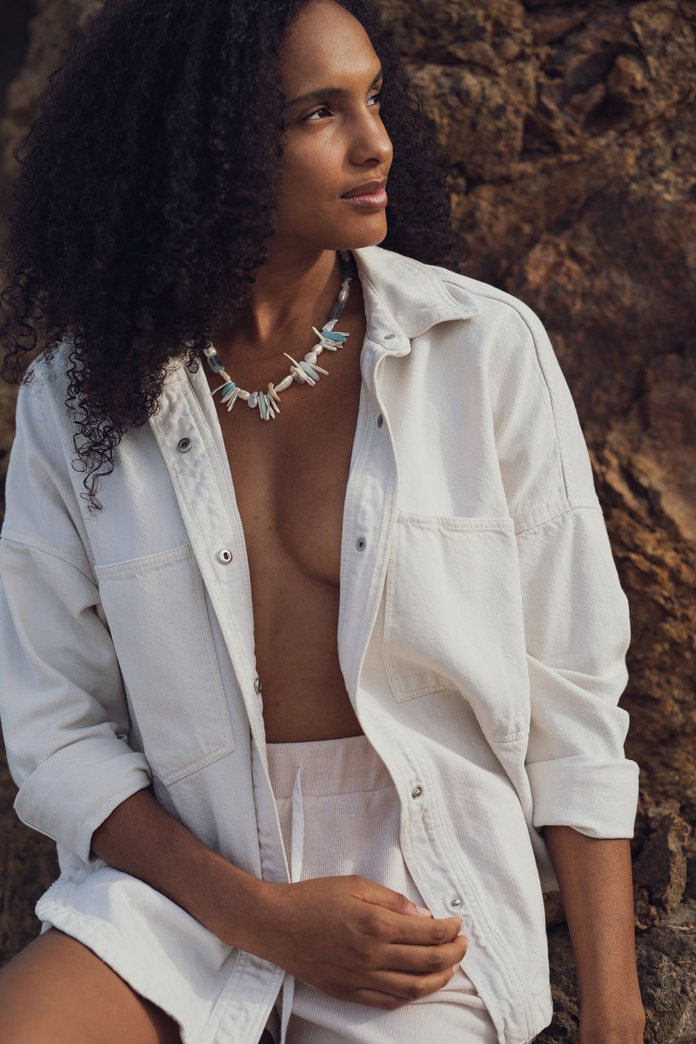 Natural light portrait showcasing bohemian style white clothing and turquoise jewelry against rocky backdrop.