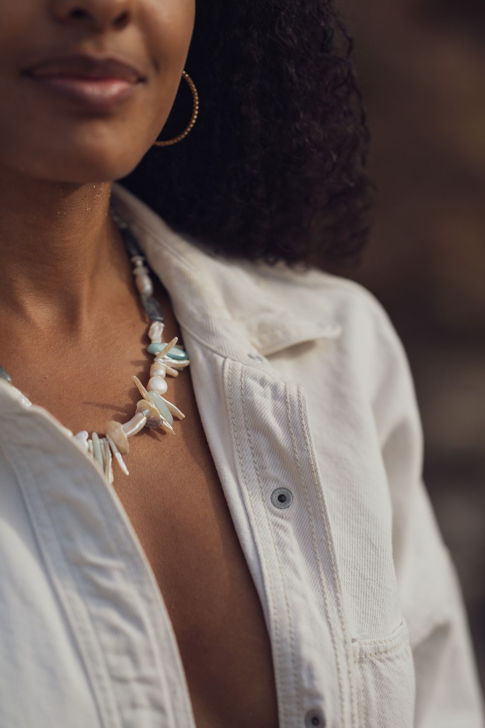 Detail shot of turquoise spike necklace and gold hoop earring with white button-down shirt.