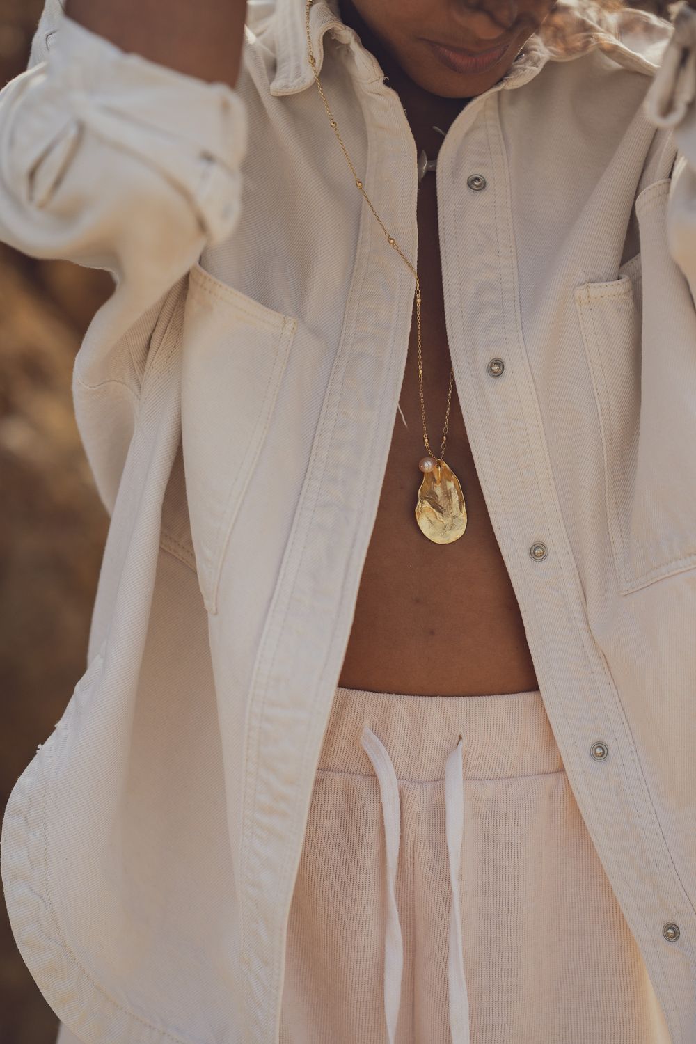 Close-up of white button down shirt with delicate gold pendant necklace and drawstring pants.