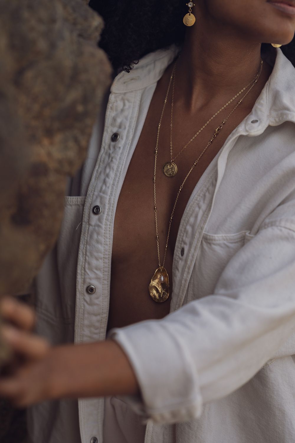Detail shot of delicate gold necklaces layered over white button-down shirt.