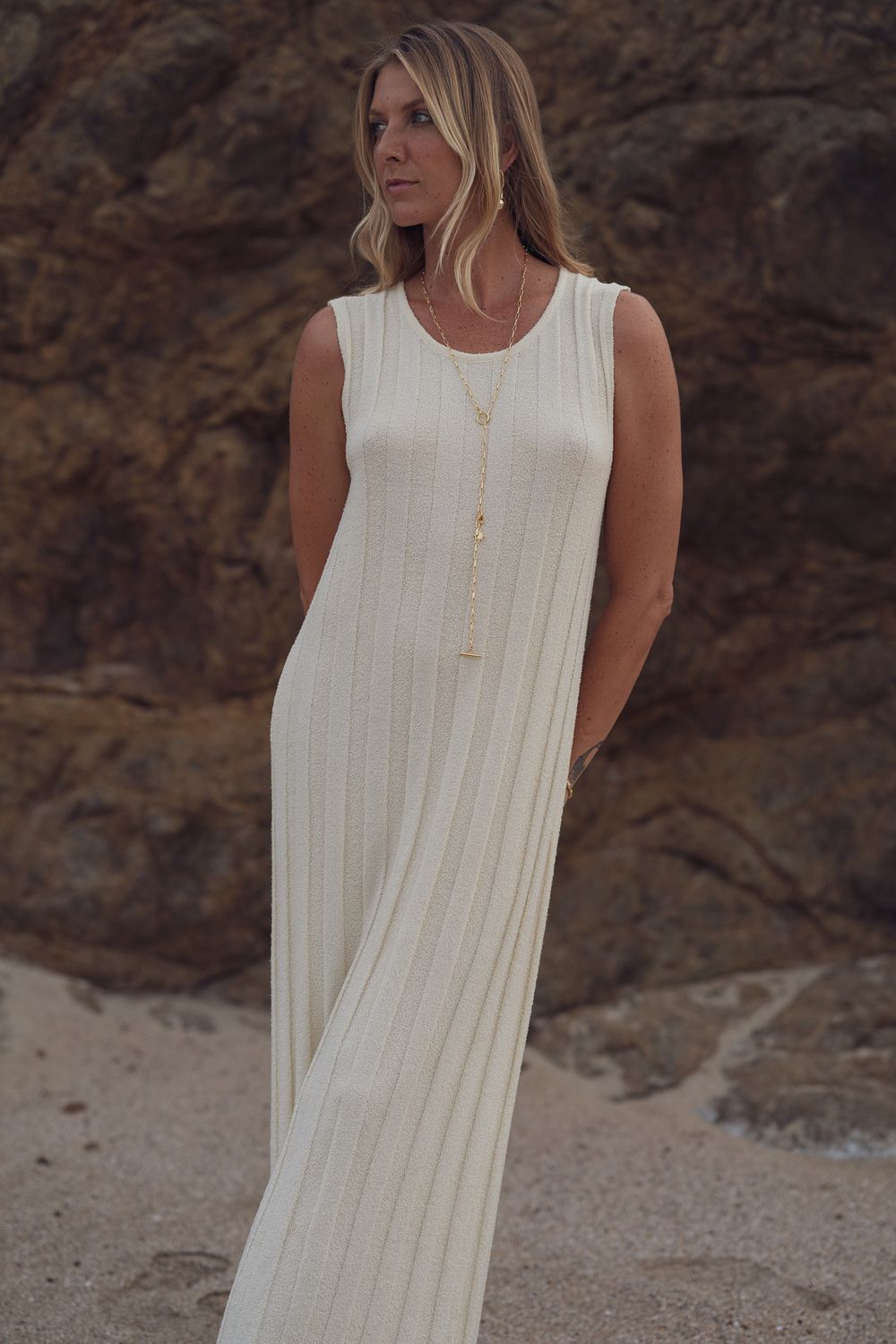 Full-length white ribbed maxi dress shown against dramatic coastal rocks.