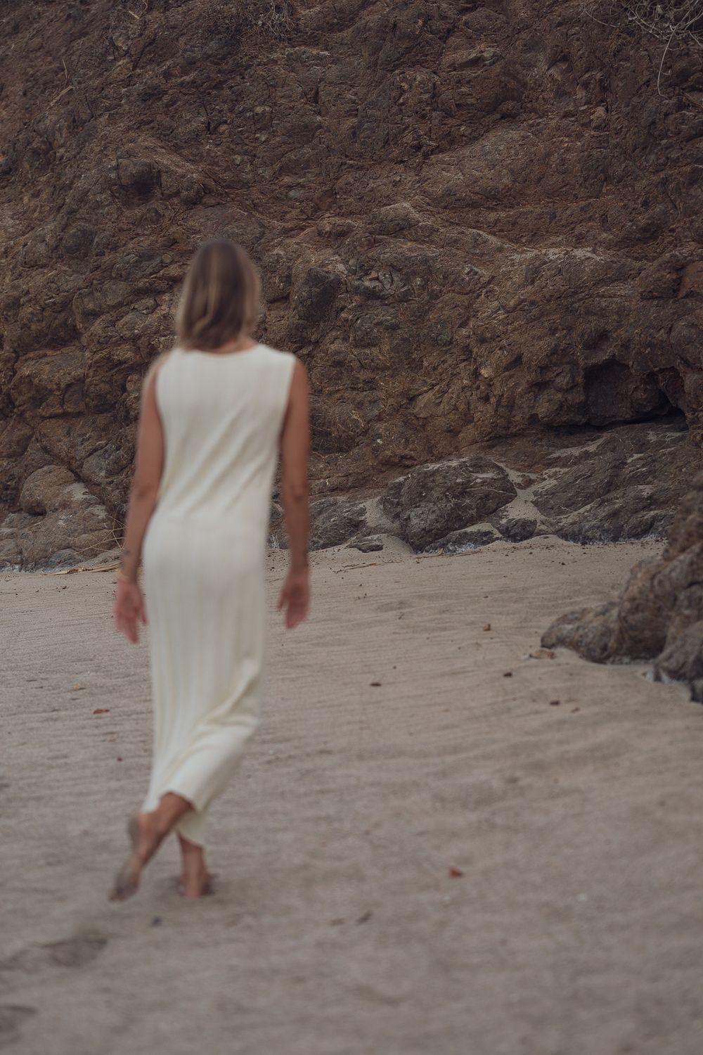 Ethereal beach scene with flowing white dress against rocky landscape.