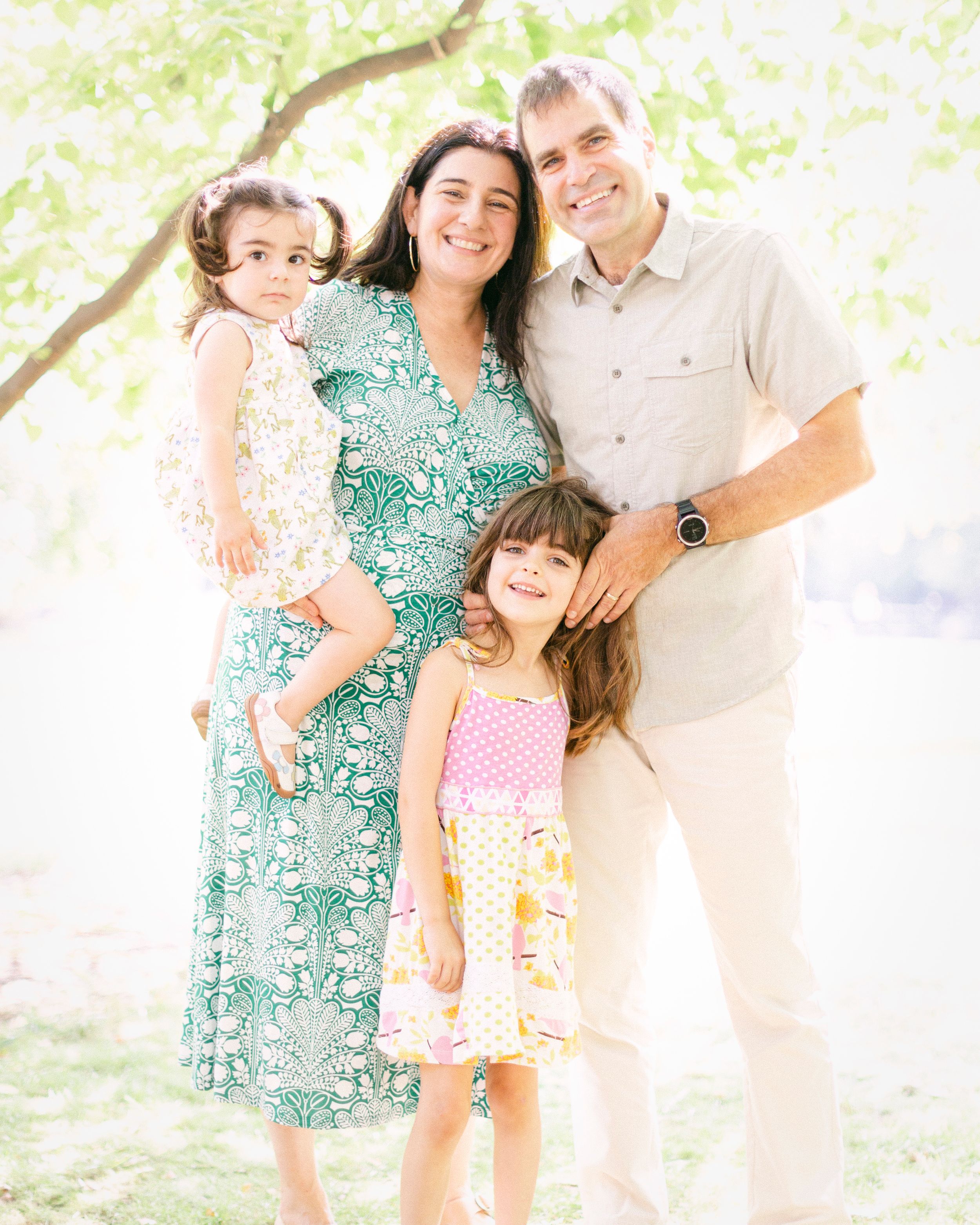 A family portrait under blooming spring trees with coordinated green and floral outfits.