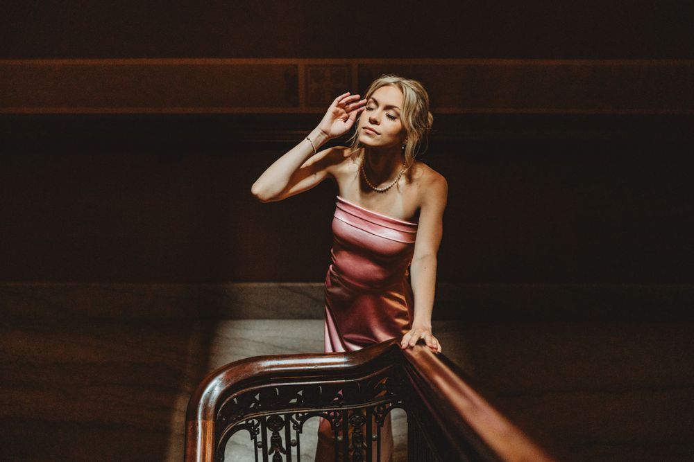 Dramatic indoor photoshoot featuring a pink satin dress against dark architectural elements.