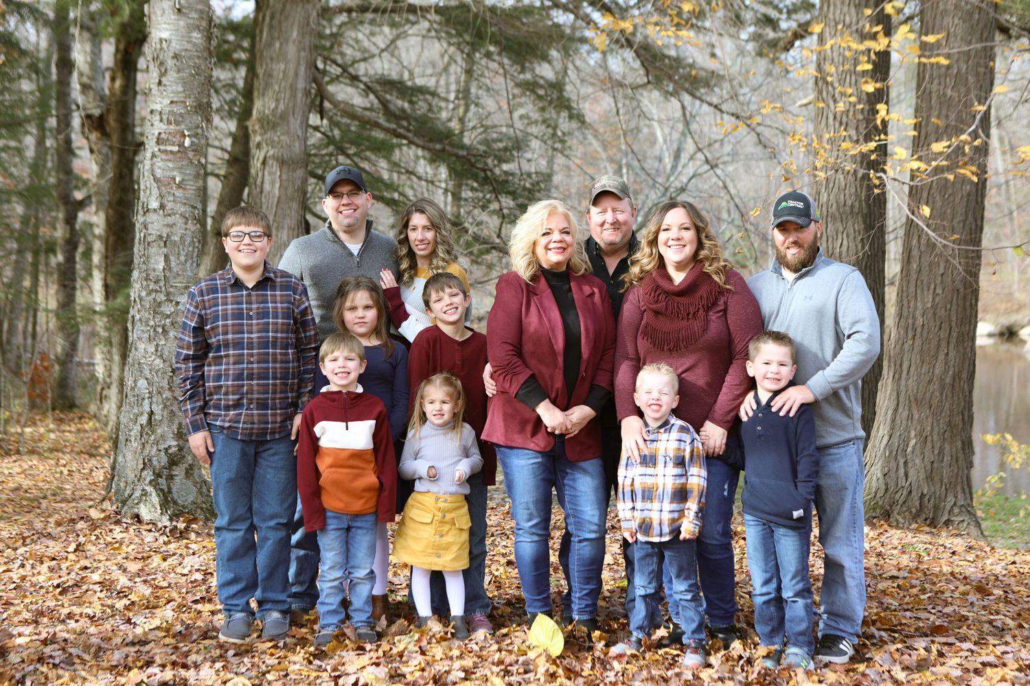 Large family group photo taken outdoors among autumn trees and fallen leaves.
