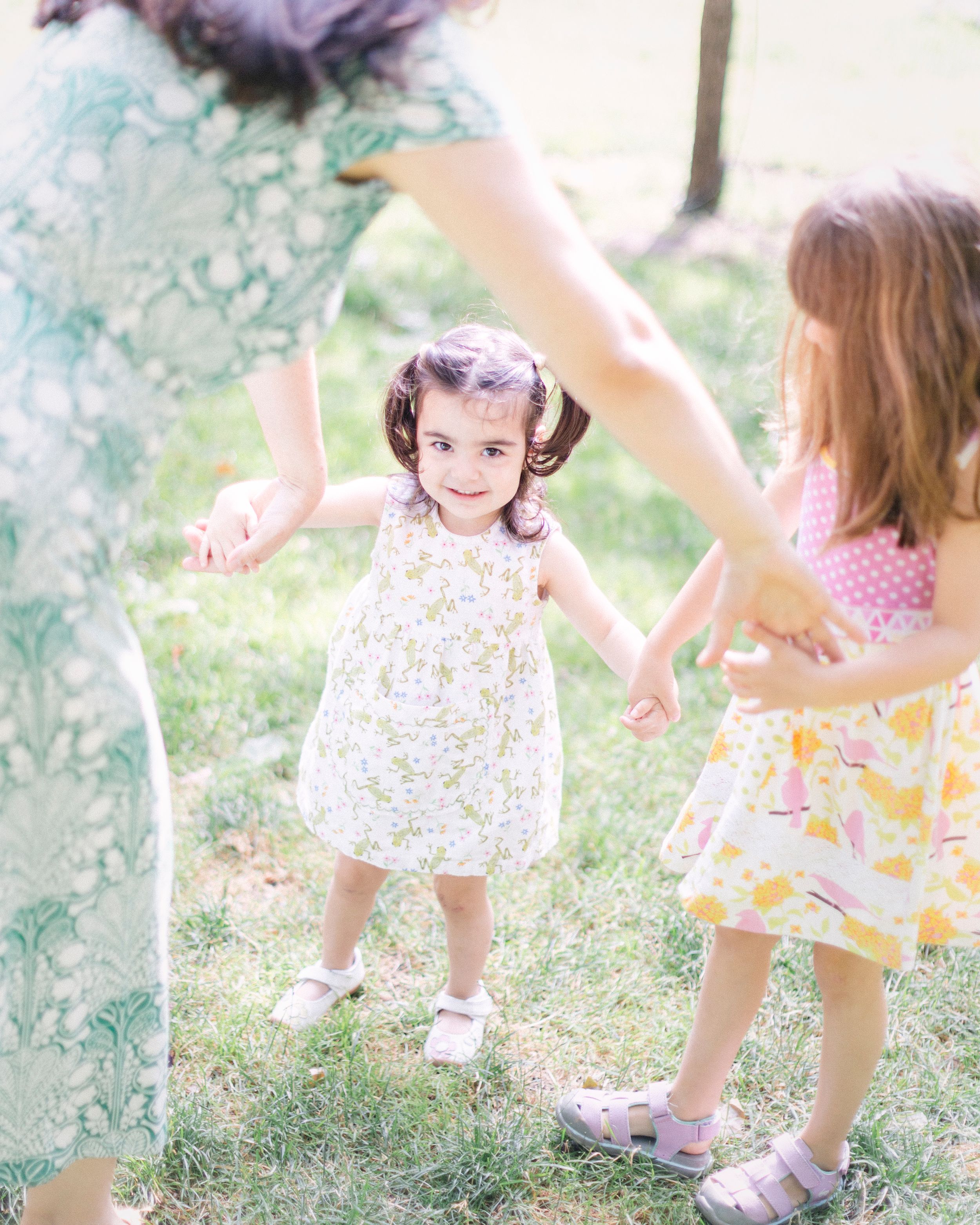 Children in floral dresses dancing and playing together outdoors in soft pastel tones.