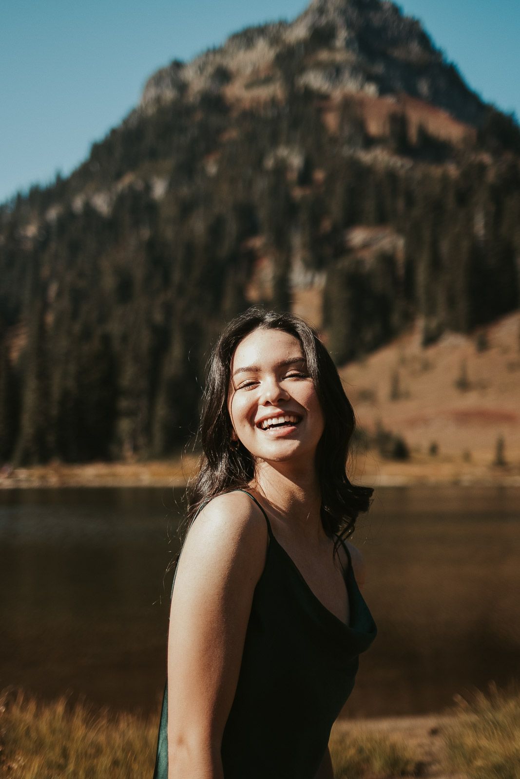 close up of smiling brown haired girl in long green silk dress in the mountains
