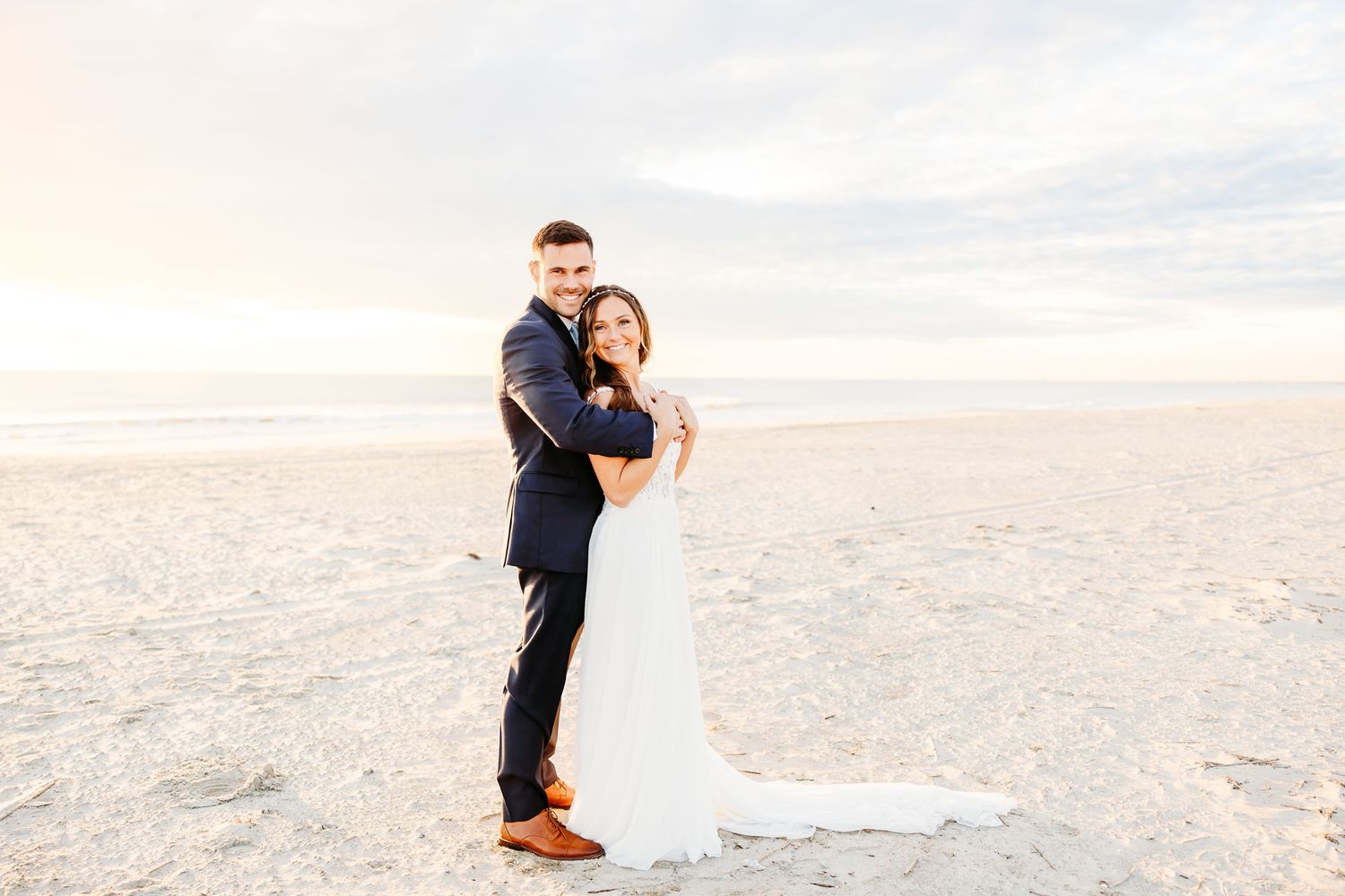 A couple shares a romantic moment on a sandy beach at sunset with ocean waves in the background.