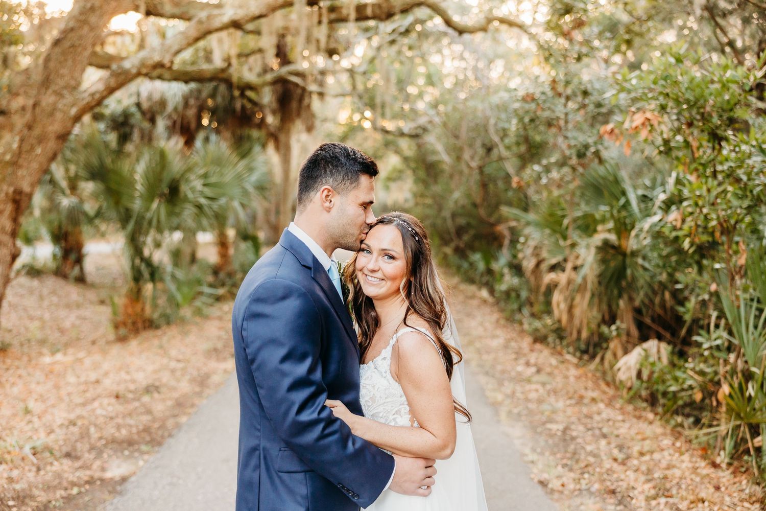 A couple shares a romantic moment surrounded by autumn leaves on a tree-lined path during their wedding photoshoot.