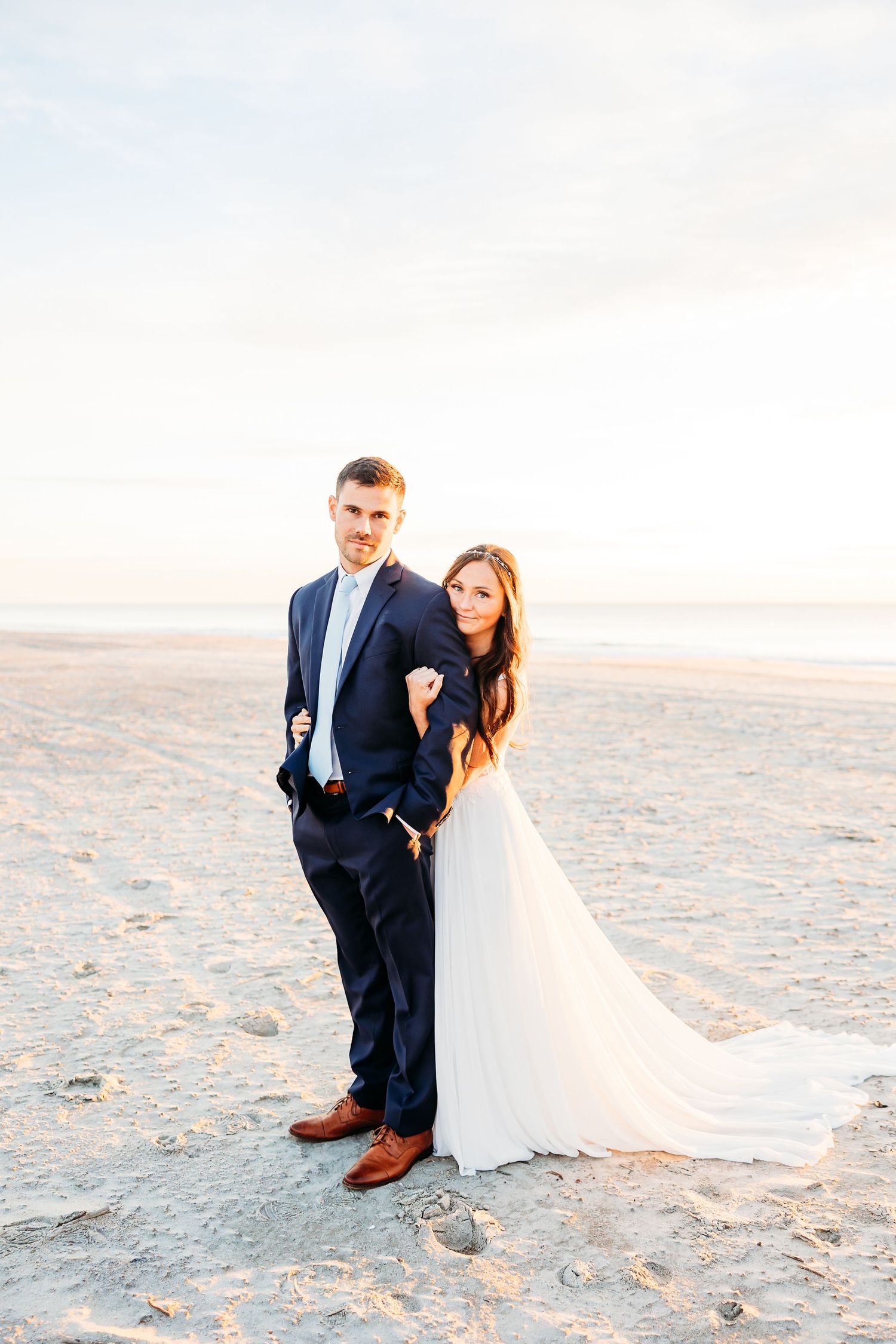 A couple in wedding attire poses together on a sandy beach at sunset in a series of romantic photos.