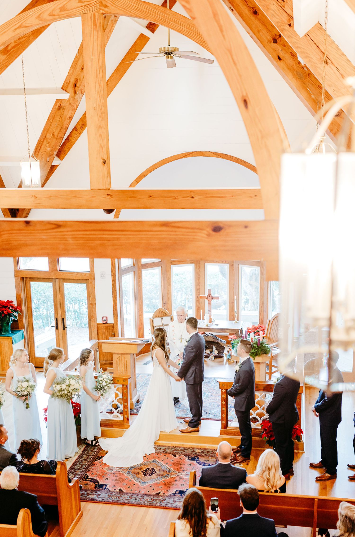 Wedding ceremony taking place in a bright timber-framed chapel with wooden beams and large windows.