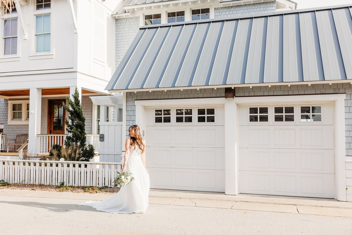 White farmhouse style garage with matching metal roof and white picket fence in front of a classic coastal home.