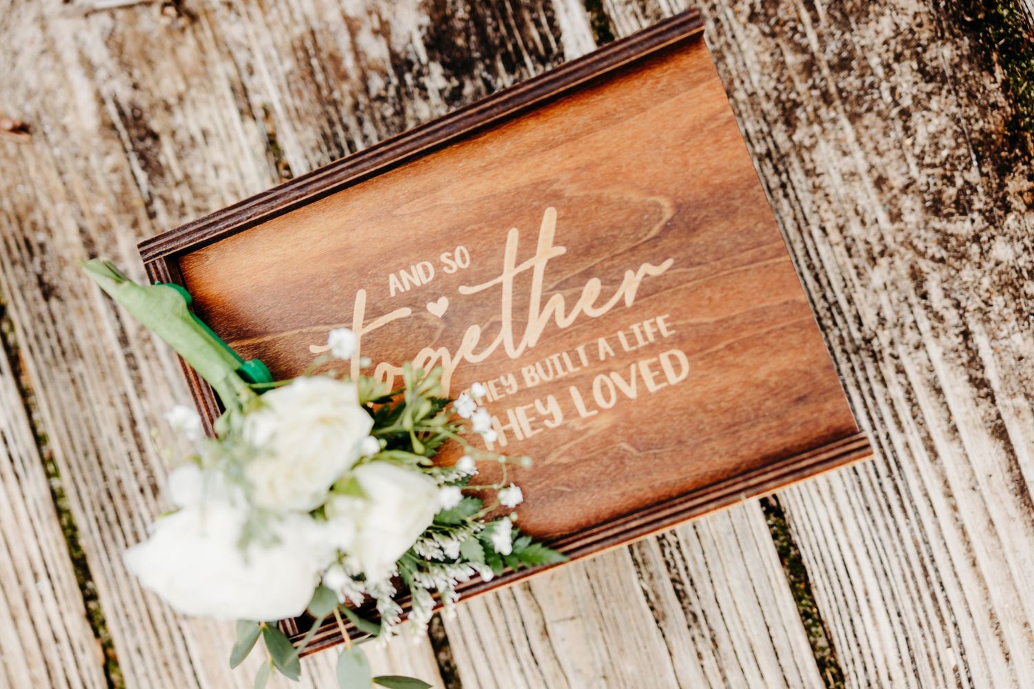Rustic wooden signs with handwritten text displayed alongside white floral decorations and greenery.