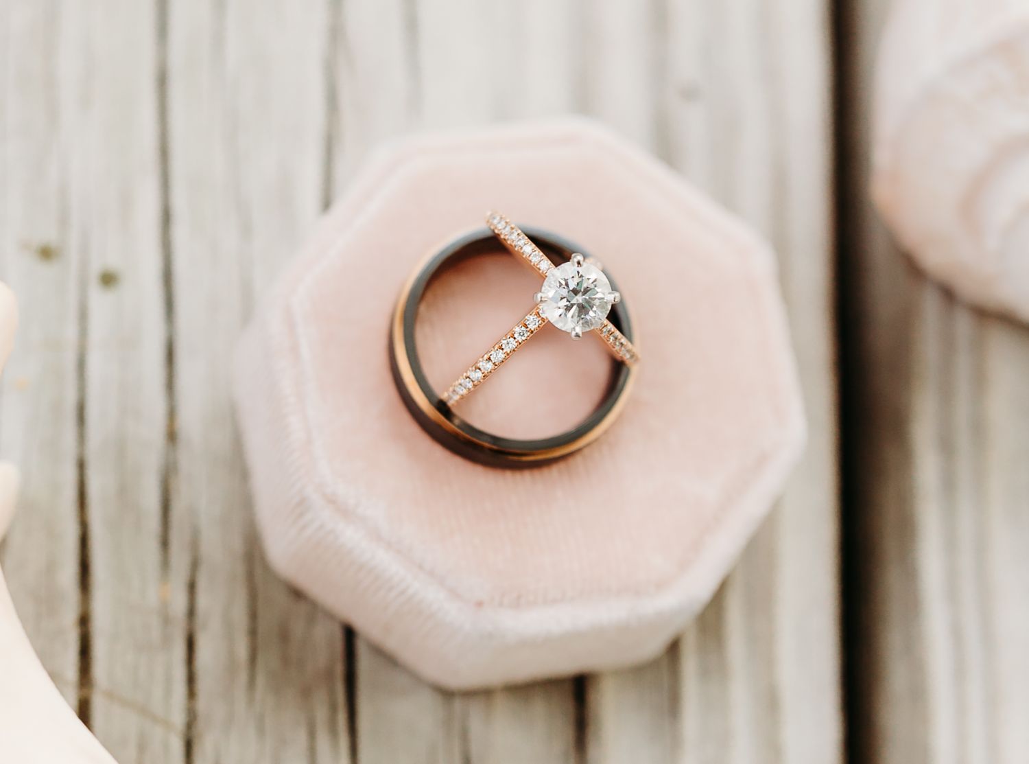 Delicate pink rose petals surround a sparkling diamond engagement ring on rustic wooden planks.