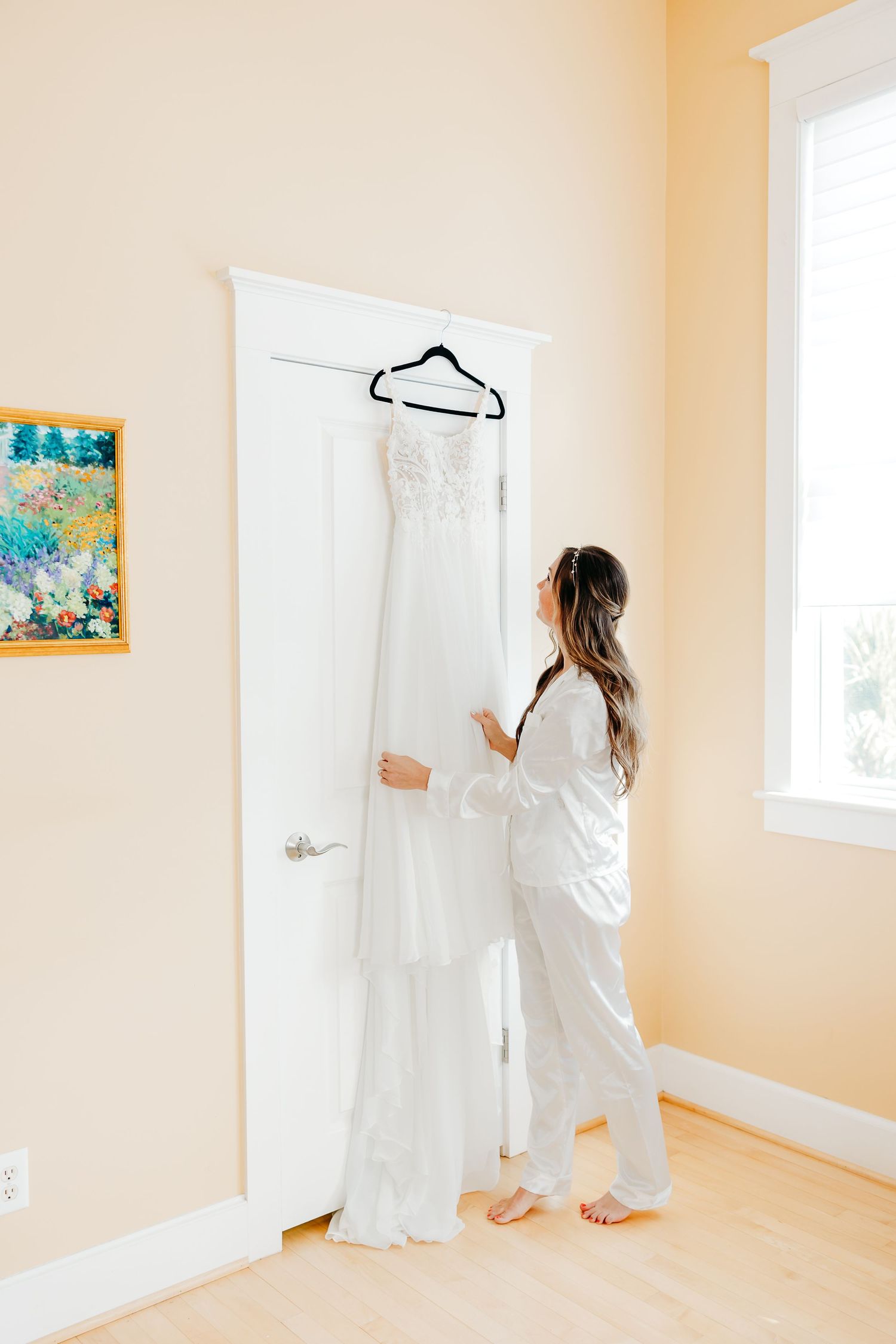 A series of images showing someone in a white dress hanging artwork on beige walls in a bright, minimalist room.