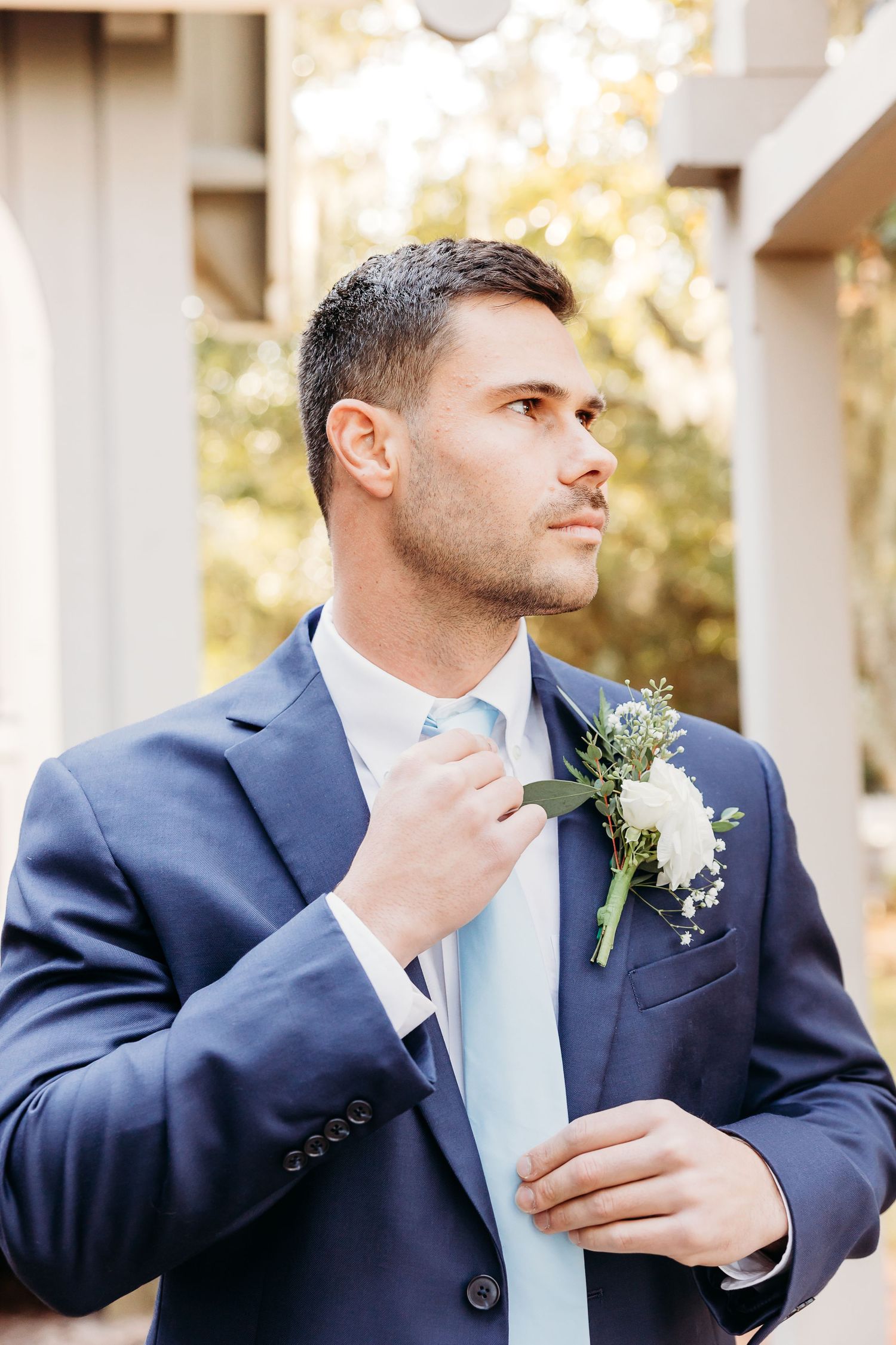 Groom in navy suit adjusts tie and boutonniere in series of profile shots during wedding preparations.