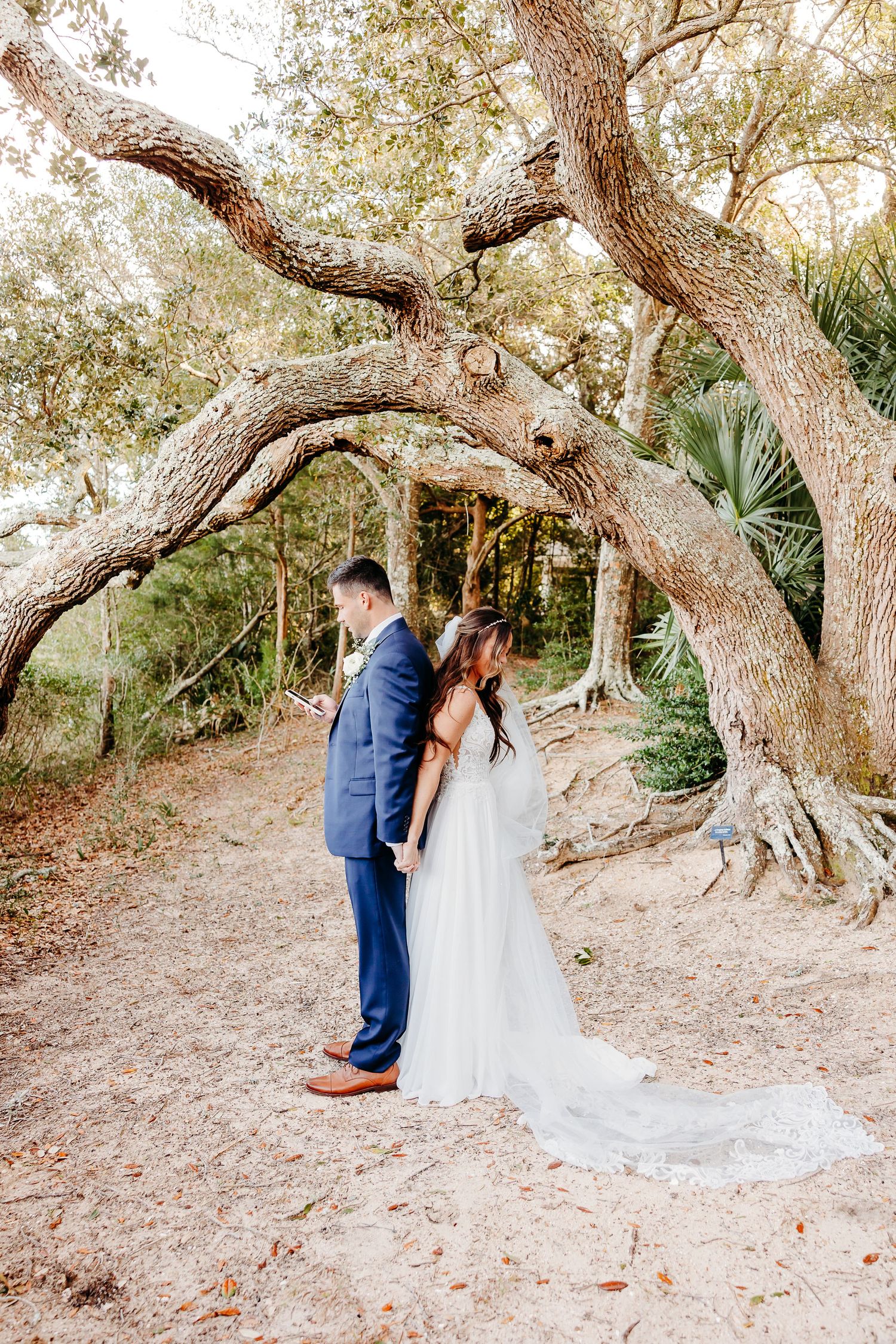 A romantic wedding couple shares tender moments under twisted oak trees in a natural outdoor setting.