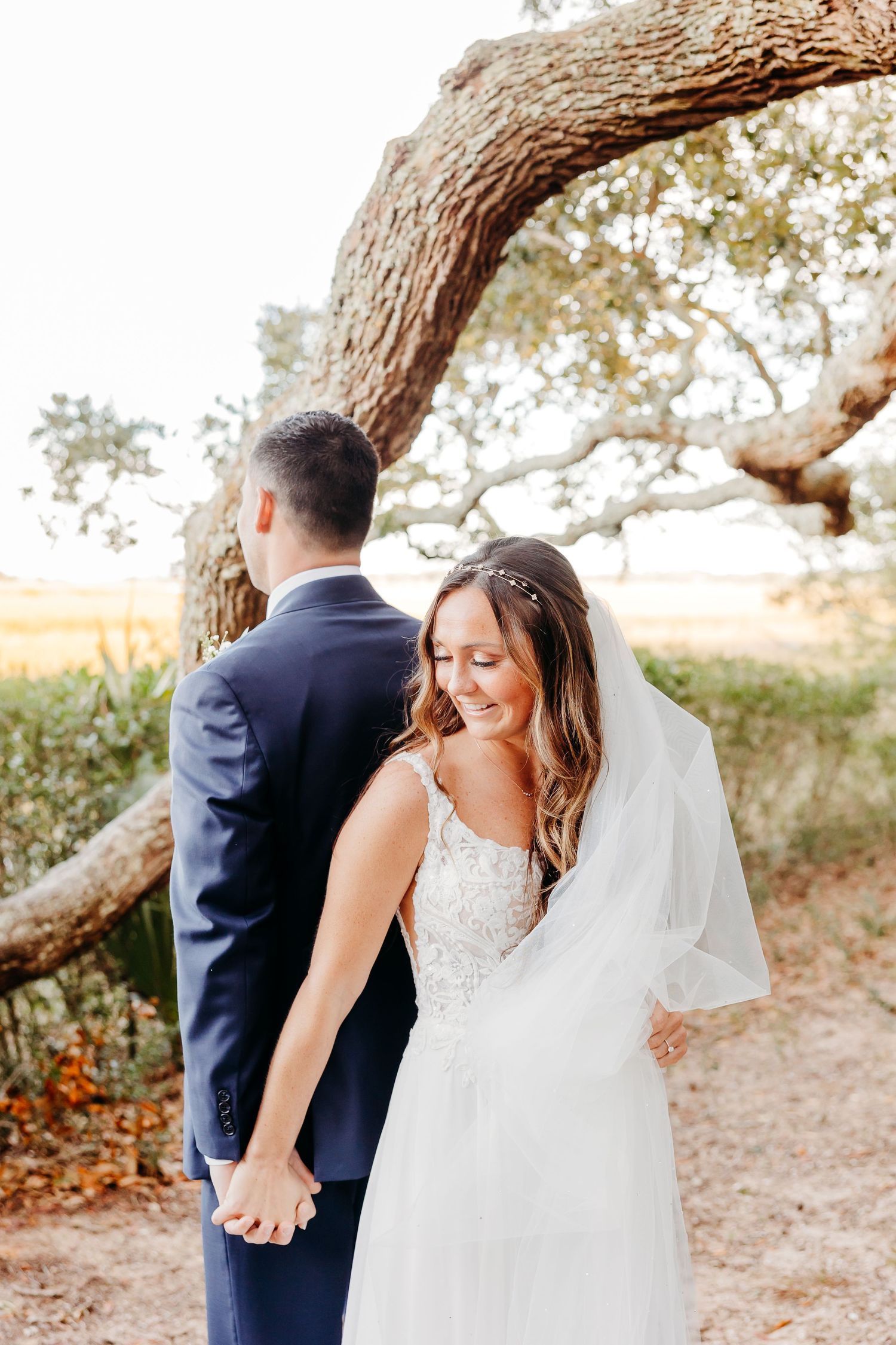 A couple in wedding attire shares a romantic moment under a tree branch during their outdoor photoshoot.
