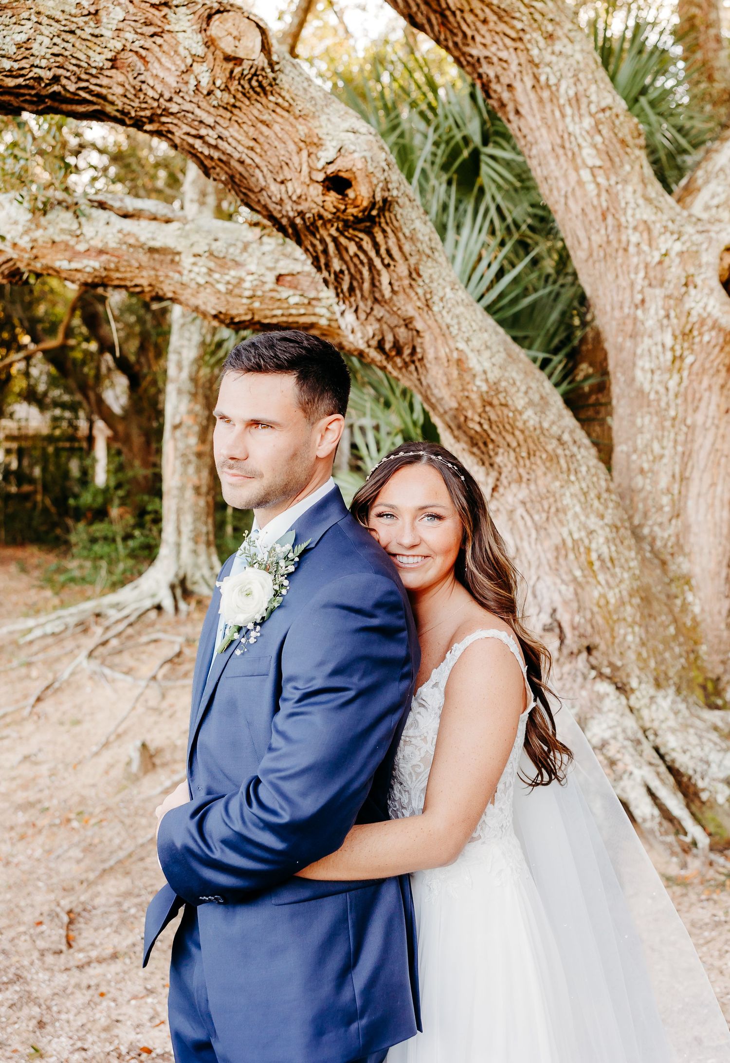 Newlywed couple poses romantically against rustic tree trunks in outdoor wedding photos.