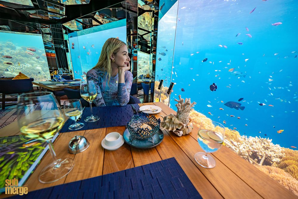Dining table setup at underwater restaurant with vibrant marine life visible through glass walls.