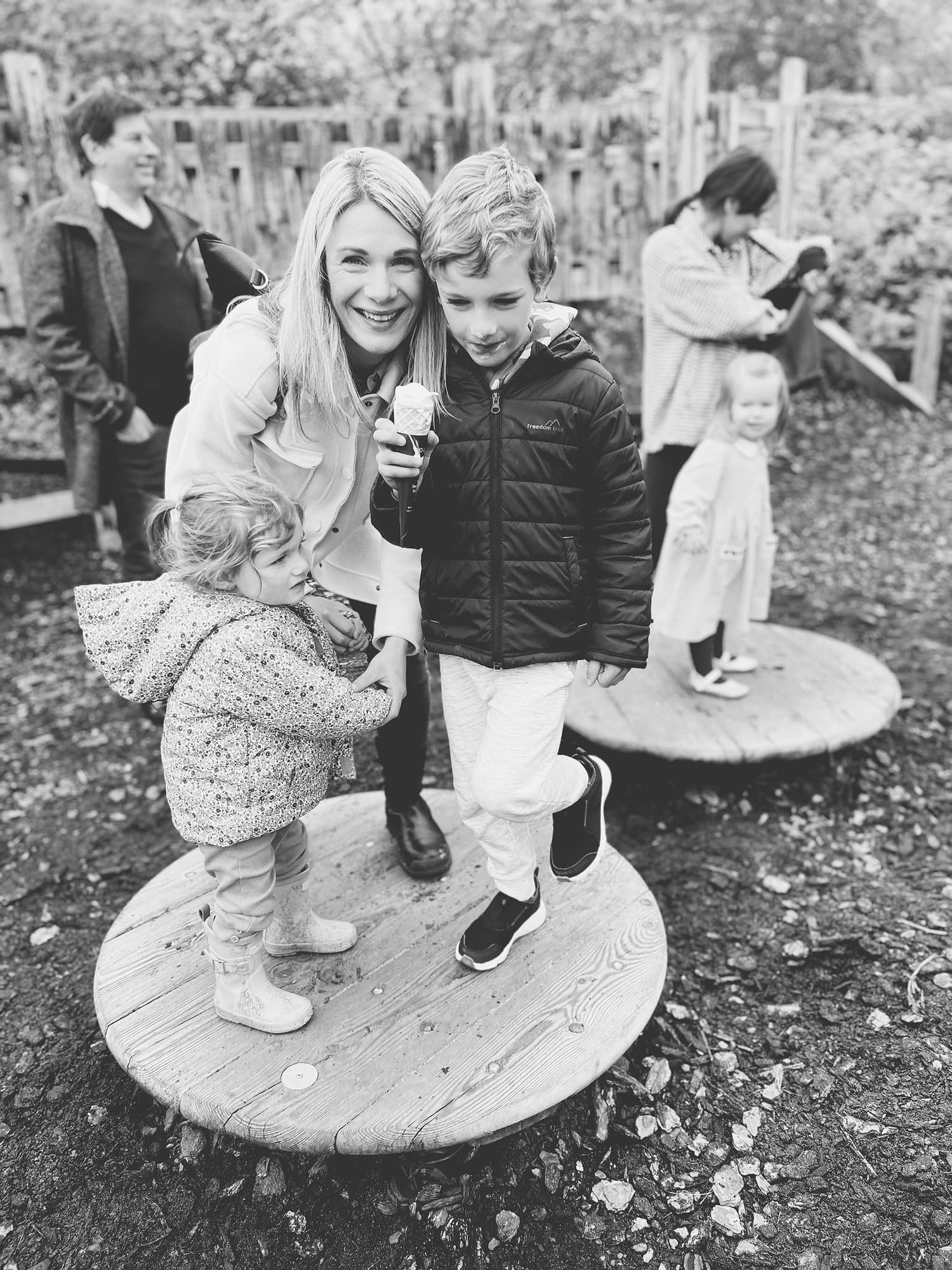 Children playing on wooden circular platforms in an outdoor garden setting.