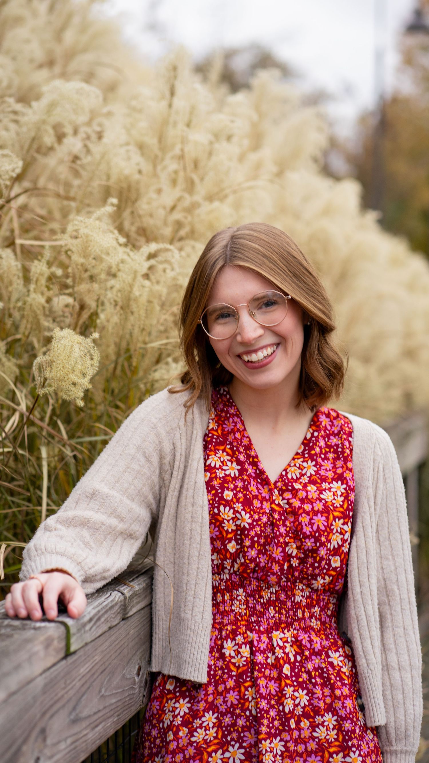 Portrait against autumn pampas grass featuring a floral dress and cozy cardigan.