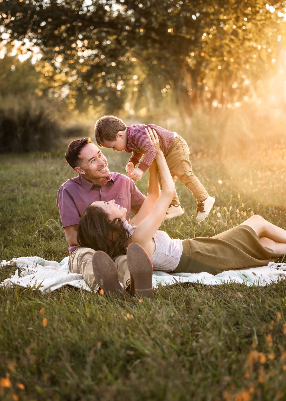 A family enjoys playful moments together on a blanket in a sunlit meadow during golden hour.