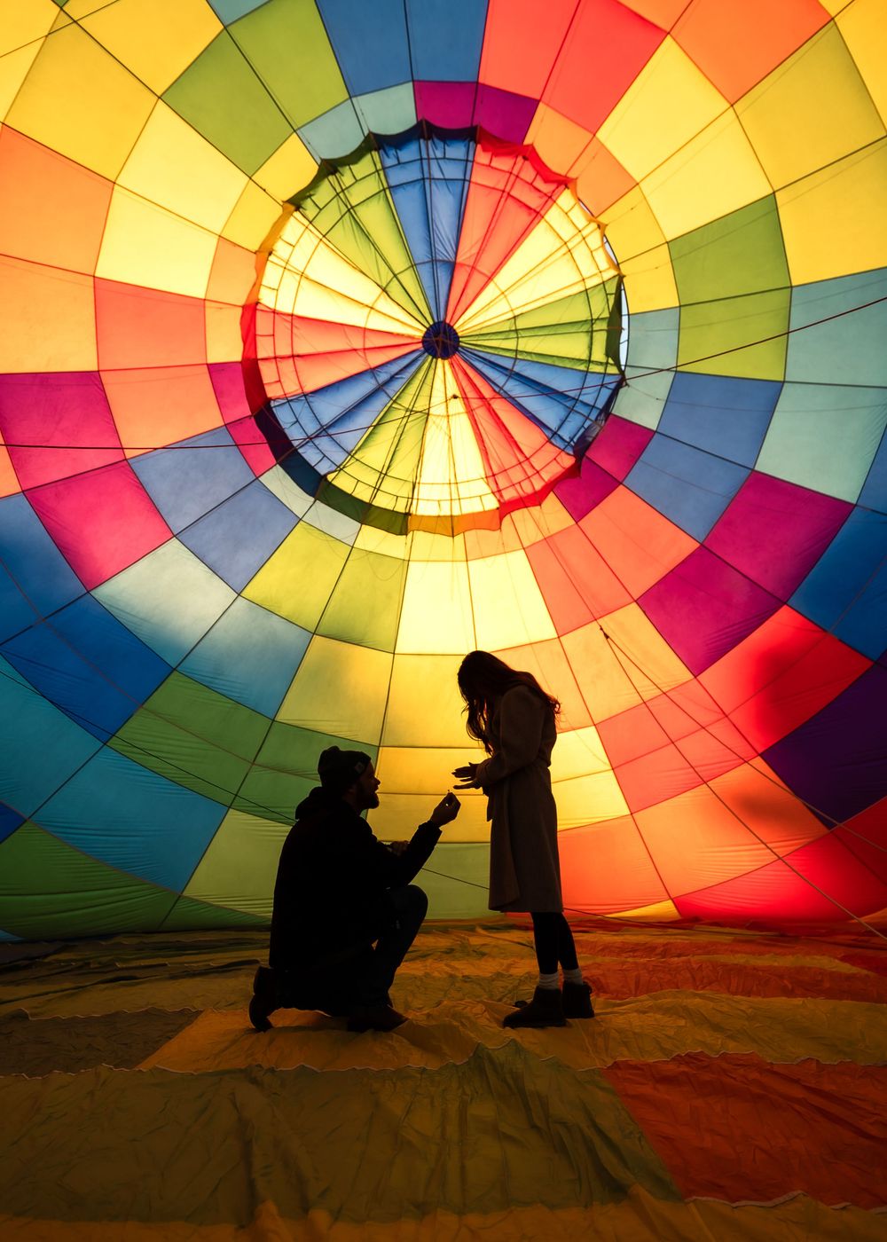 Silhouettes of people against a vibrant rainbow-colored hot air balloon canopy during preparation for flight.