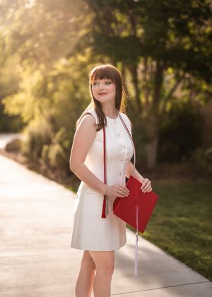 A person in a white dress carrying a red handbag walks along a sunlit path with trees in the background.