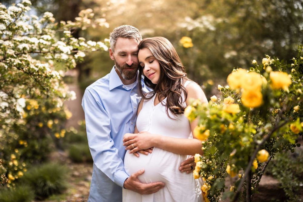 A couple shares tender embraces in a sunlit garden with blooming yellow flowers.