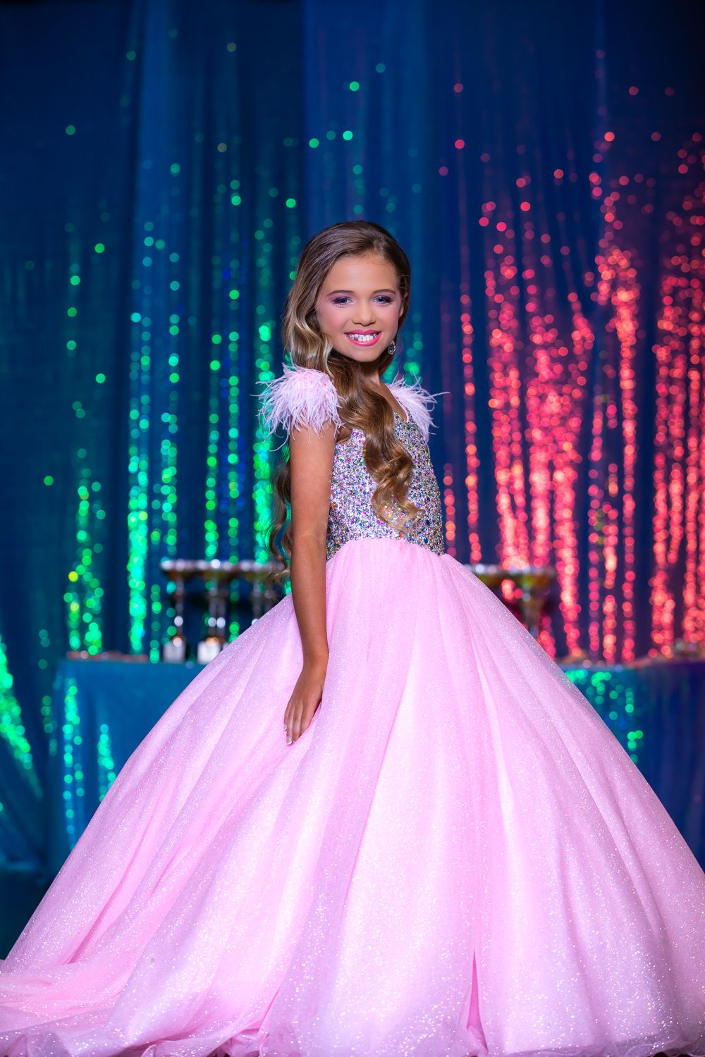 Princess style ball gown in pink with feather details against colorful light display.