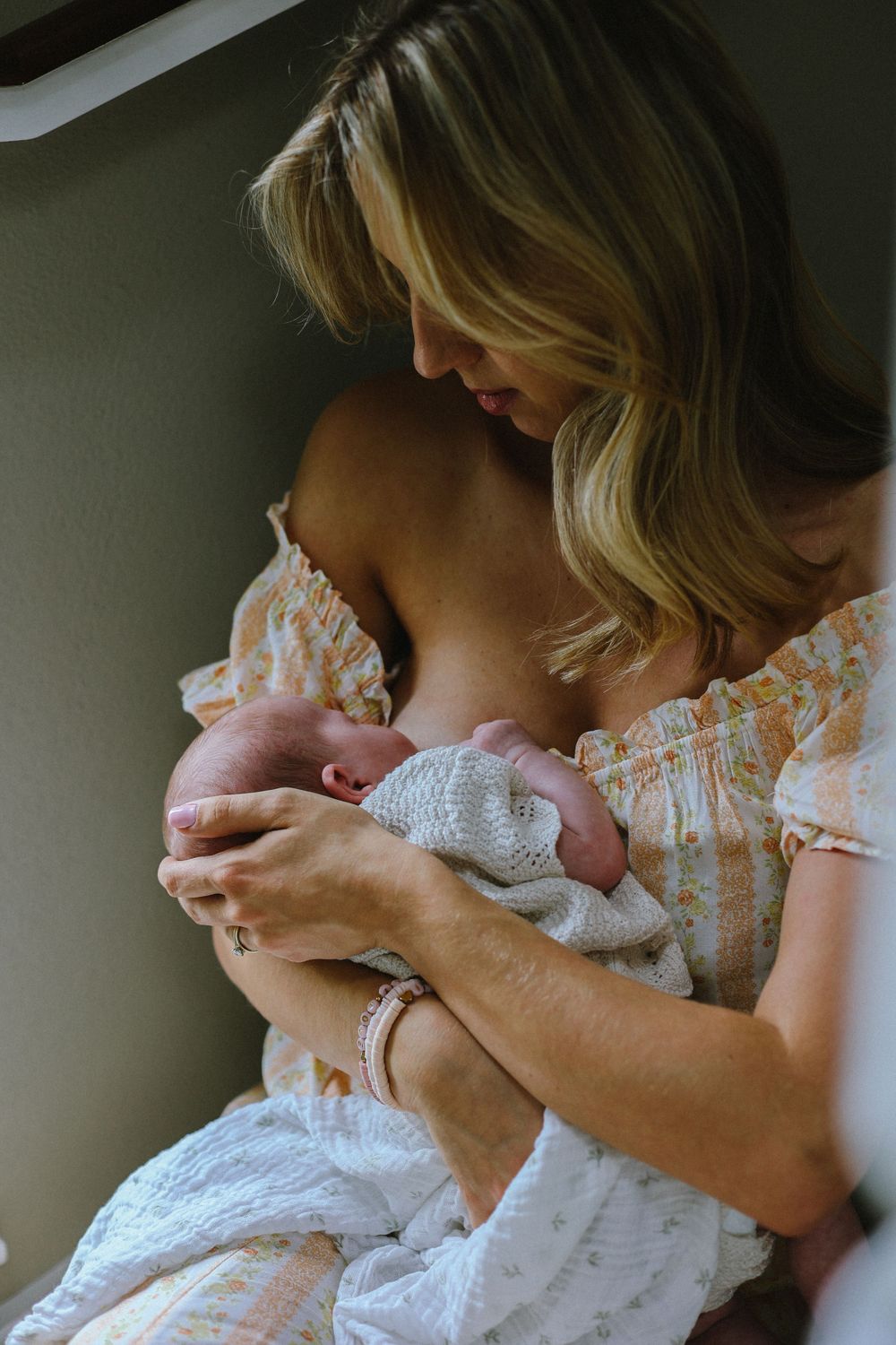 A tender moment as a parent in a floral dress cradles and gazes down at their newborn baby wrapped in white.