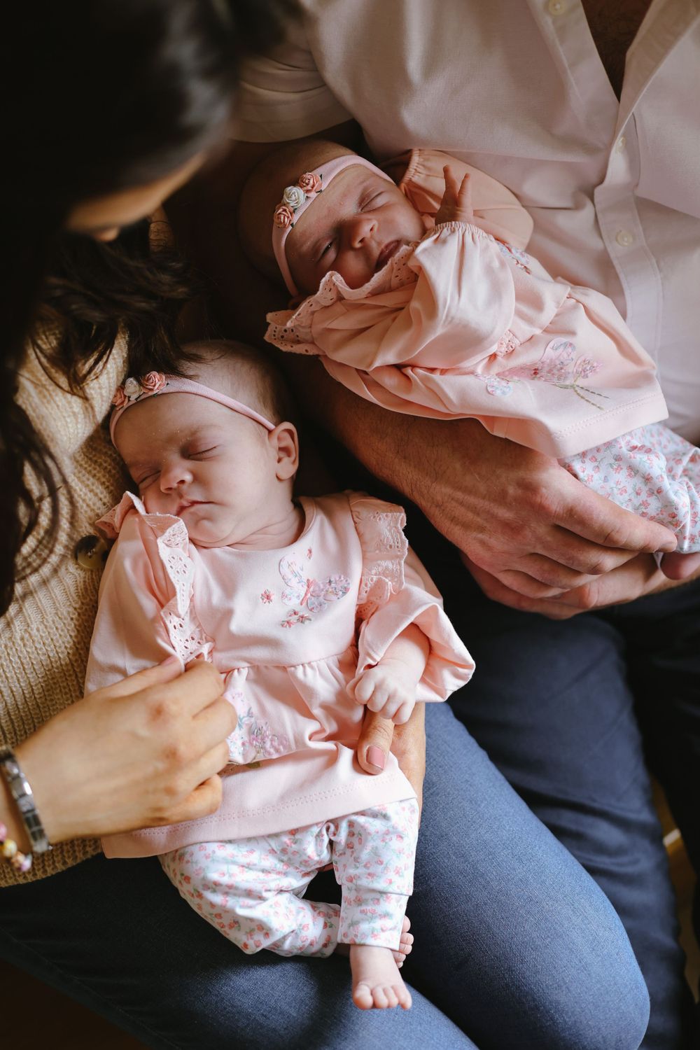 Two infant twins in matching pink outfits rest on their caregiver's lap.
