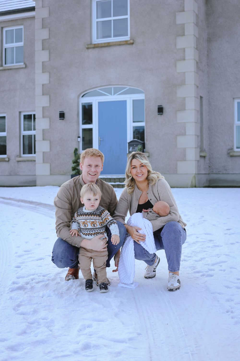 A family poses together in the snow in front of their house with a bright blue door.
