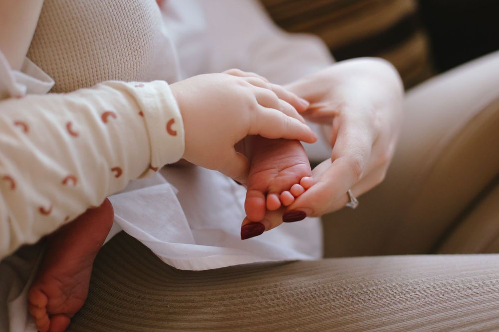 Close-up of tiny baby feet being gently held by caring hands on a soft white surface.