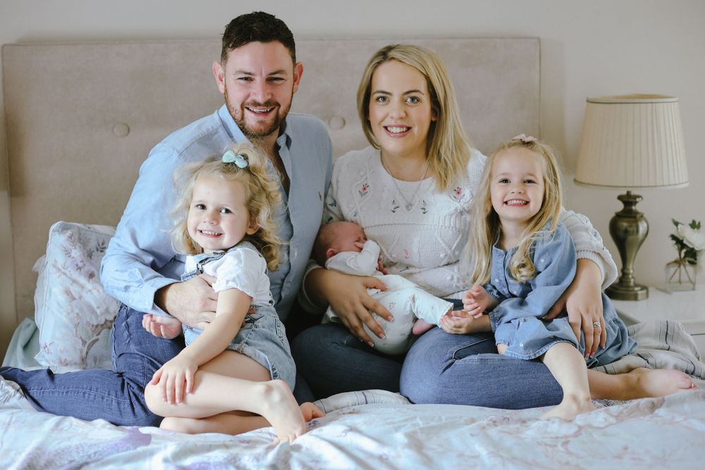 A happy family relaxes together on a bed, including young children and a newborn baby.