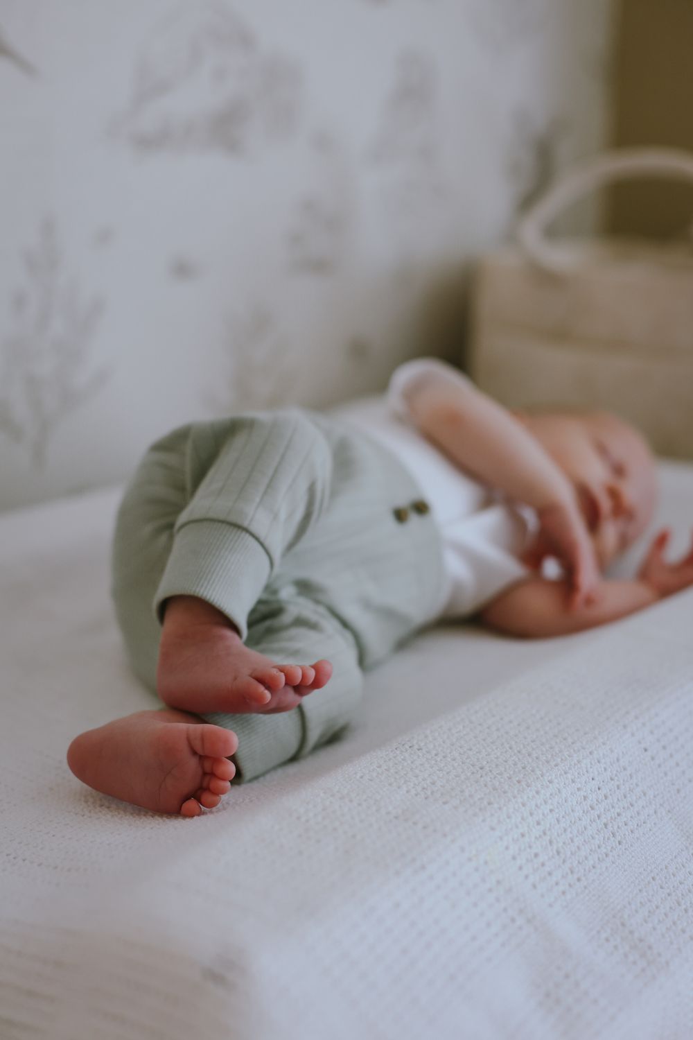 Close-up view of tiny baby feet and legs resting on white textured fabric in soft natural lighting.