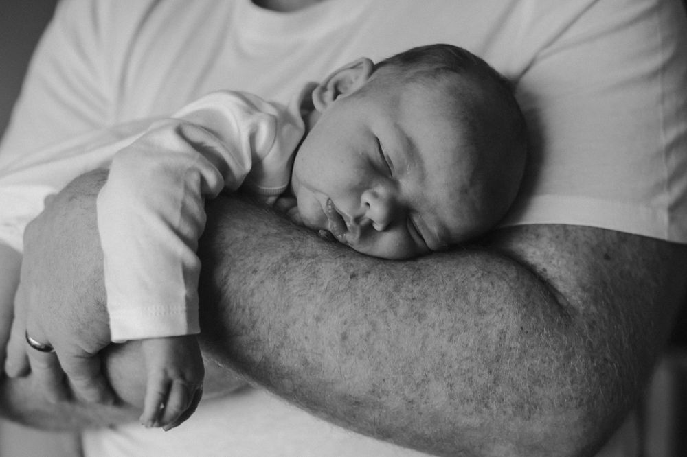 A sleeping infant rests peacefully on an adult's arm in black and white.