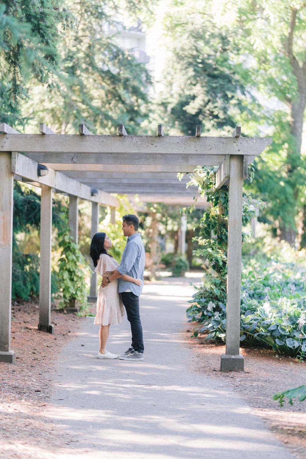 A couple shares an intimate moment under a wooden pergola in a garden path.