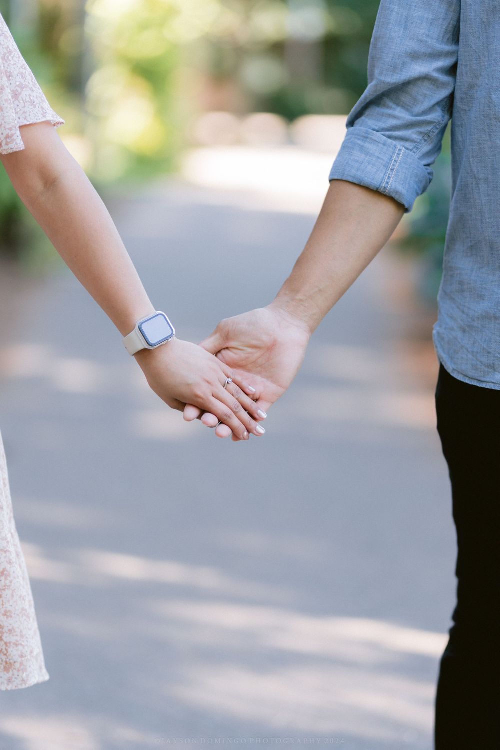 Close-up of two people holding hands while wearing casual attire outdoors.