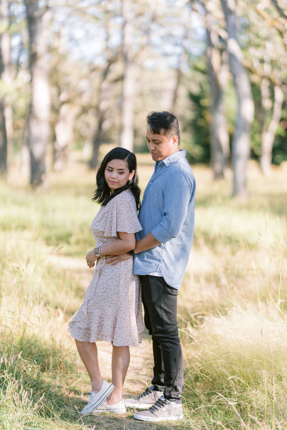 A romantic couple pose together in a sun-dappled forest clearing.