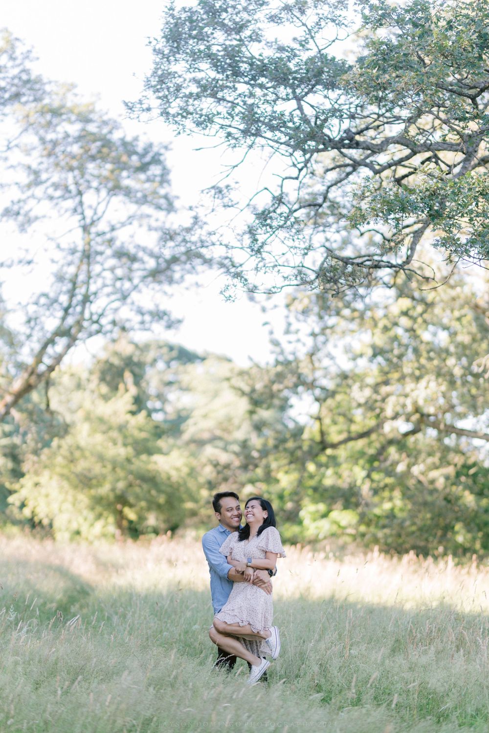 Romantic couple sharing a moment in a sunlit field with trees in the background.
